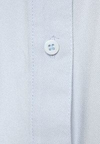 Light blue fabric with a fine, textured weave. Features a white button with two holes, stitched with matching thread along the edge.