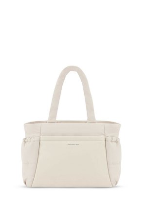 Personne portant un sweat à capuche crème et des leggings noirs, portant un grand sac fourre-tout beige rembourré sur l'épaule.