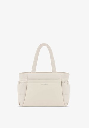Personne portant un sweat à capuche crème et des leggings noirs, portant un grand sac fourre-tout beige rembourré sur l'épaule.