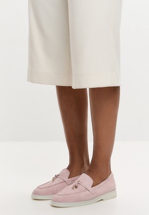 Nogi w białych spodniach do kolan i jasnoróżowych zamszowych mokasynach z małymi złotymi i skórzanymi frędzlami.