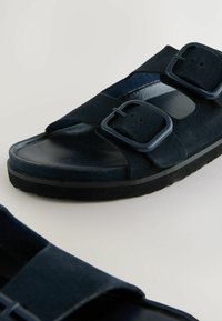 Sandalias de color azul marino hechas de ante y goma, con dos hebillas ajustables y una puntera suave y brillante.
