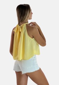 Top giallo senza maniche con colletto halter e dettaglio a fiocco, caratterizzato da una vestibilità ampia e tessuto leggero, abbinato a pantaloni corti in denim bianchi.