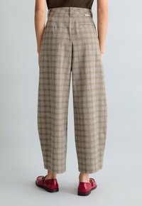 Karierte braune Hosen mit weitem Bein, hoher Taille, Seitentaschen und einer Gesäßtasche, kombiniert mit roten Schuhen mit einer kleinen Schleifendetail.