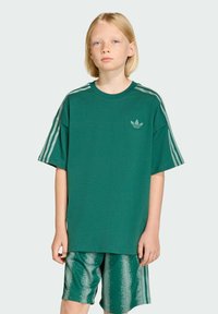 Zelené tričko z bavlny s krátkymi rukávmi a okrúhlym výstrihom; obsahuje tri biele pruhy na pleciach a malé logo na hrudi. Zelené vzorované šortky.