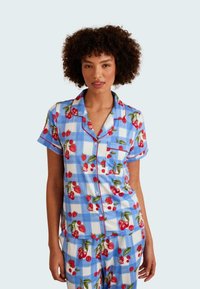 Light blue plaid pajama set with cherry patterns, short sleeves, and red trim. Features a button-up top and matching bottoms with pockets.