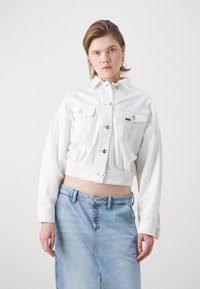 Kratka bela jeans jakna z gumbi, dvema sprednjima žepoma in elastiko pri pasu, v kombinaciji s svetlo modrim denim krilom.