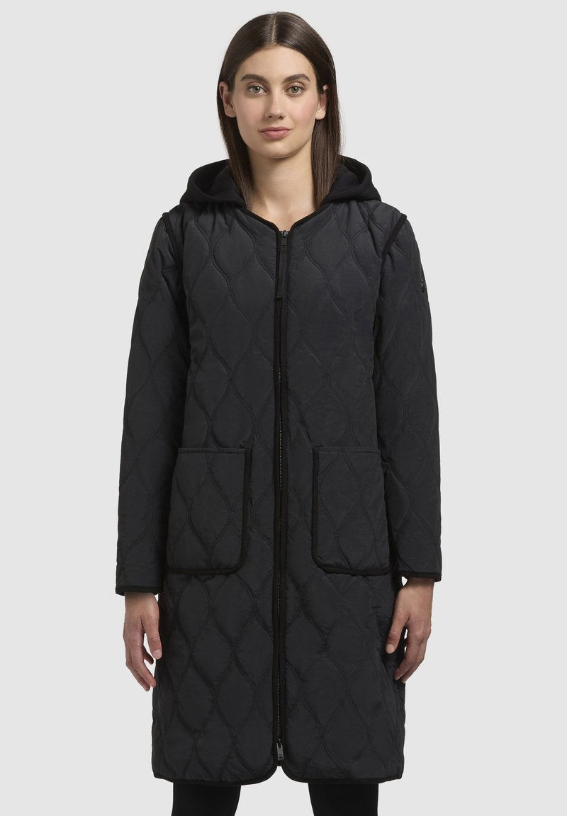 Cappotto lungo trapuntato nero con zip frontale, cappuccio e due grandi tasche. Texture liscia con un motivo a rombi e piping a contrasto.