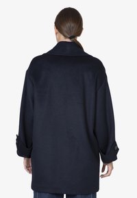 Cappotto oversize blu navy con colletto, maniche lunghe e polsini con bottoni. La texture morbida e le linee pulite creano un design minimalista.