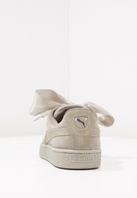 Puma tenisky v světle béžové semišové úpravě s texturovaným zadním dílem, velkými saténovými tkaničkami ve tvaru mašle a kulatou logopatchí na patě.