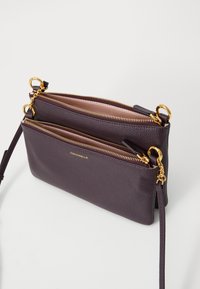 Borsa a tracolla in pelle viola con due scomparti con zip, dettagli in hardware dorato e finitura testurizzata. Include una tracolla regolabile.