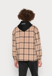 Rutigt flanelljacka i beige, brunt och orange, med en svart huva. Löst skuren, med långa ärmar och knäppningar vid ärmsluten.