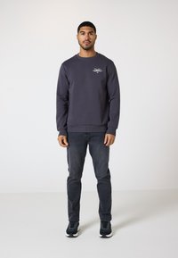 Mørkegrå sweatshirt med rund hals og ribbestrikkede manchetter, prydet med et lille hvidt logo. Sættes sammen med mørke jeans og sorte sneakers.