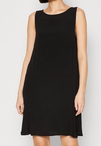 Robe noire sans manches avec un col rond, fabriquée en tissu lisse, légèrement évasée au niveau de l'ourlet et offrant une coupe décontractée.