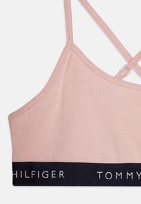 Sujetador rosa claro con un diseño sencillo, que presenta tirantes finos y una banda azul marino con texto en blanco. Tejido suave con una cinturilla elástica.