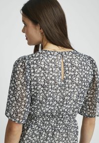 Robe à motifs floraux en tissu transparent marine avec des fleurs blanches, manches courtes bouffantes et détail de dos en trou de serrure.