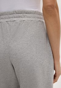 Graue Sweatpants mit einer weichen, strukturierten Oberfläche. Merkmale einen elastischen Bund und einen schmalen, taillierten Schnitt, von hinten gezeigt mit einer Hand auf der Hüfte.