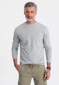 Harmaa pitkähihaisen t-paita, joka on valmistettu pehmeästä kankaasta, jossa on pyöreä pääntie ja slim fit -mukautus, yhdistettynä oliivinvihreisiin housuihin ja kelloon.