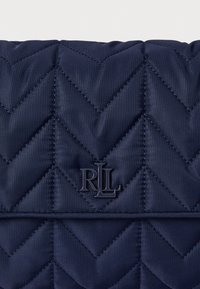 Τσάντα από ναυτικό καπιτονέ ύφασμα με σχέδιο σχήματος κεβρόν, διαθέτοντας υφή και ανάγλυφο λογότυπο "RLL" στην κάτω γωνία.