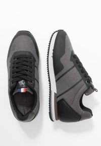 Baskets de sport noires et grises en matériaux mesh et cuir, bout rond, motifs texturés contrastés et semelle blanche. Détails des lacets et du logo inclus.