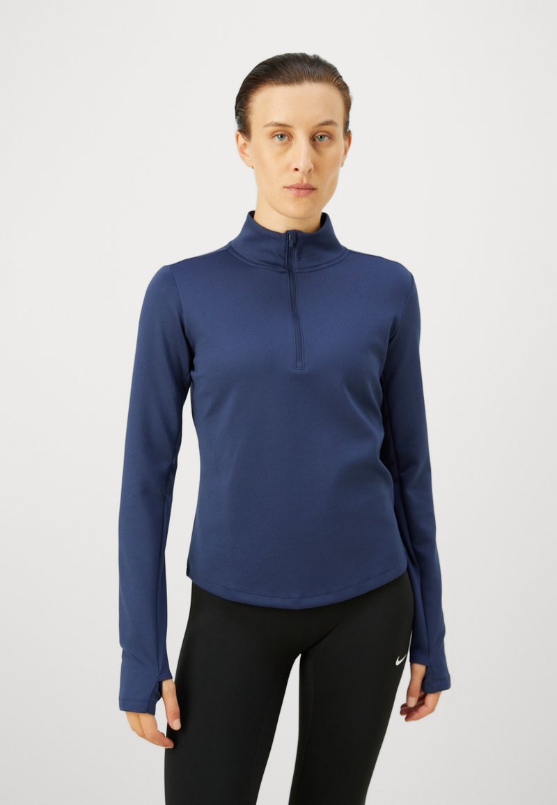 Marineblå langærmet zip-up top lavet af strækbart materiale, med en mock krave, flade sømme og tommelhuller ved ærmerne, kombineret med sorte leggings.