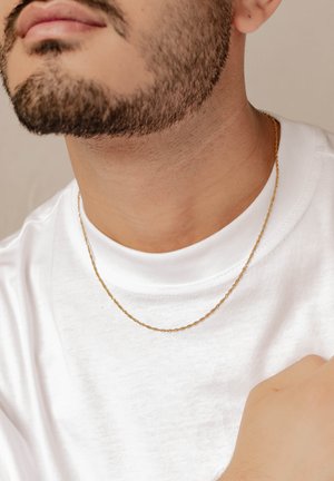 Goldene Kettenhalskette mit einem verdrehten Design, die auf einem nackten Hals ruht, kombiniert mit einem schlichten weißen T-Shirt. Glatte Textur, minimalistischer Stil.
