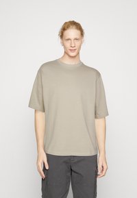 Katoenen T-shirt in lichtbeige, ronde hals, korte mouwen, boxy fit, gladde textuur, gecombineerd met donkere cargo broek.