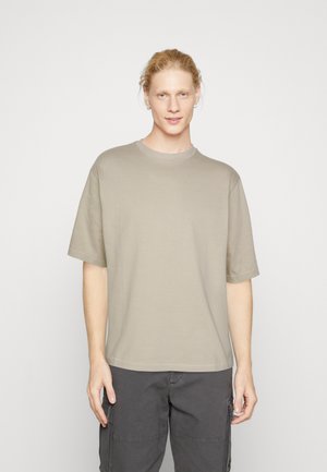 Cotton t-shirt in light beige, crew neck, short sleeves, boxy fit, smooth texture, paired with dark cargo pants.