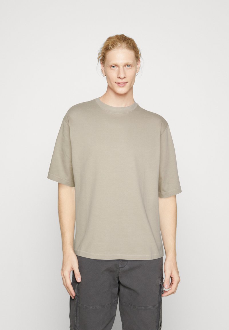 Katoenen T-shirt in lichtbeige, ronde hals, korte mouwen, boxy fit, gladde textuur, gecombineerd met donkere cargo broek.