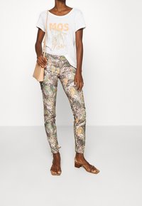 Witte katoenen t-shirt met "MOS" graphic, gecombineerd met smalle, multicolor dierenprint broek en beige sandalen met bandjes. Inclusief een tan crossbody tas.