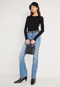 Zwarte top met lange mouwen, lichtblauwe hooggetailleerde spijkerbroek, zwarte riem met ronde gespen, zwarte getextureerde handtas met zilveren studs, en zwarte laarzen met hak.