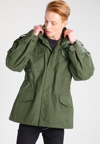 Geacă parka verde oliv cu închidere cu fermoar, două buzunare laterale și șnur ajustabil la talie; realizată dintr-un material durabil.
