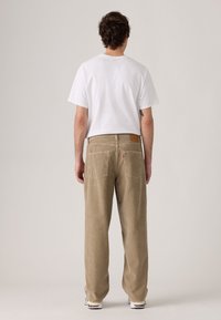 Beige corduroy pants, loose fit, featuring back pockets and a leather label on the waistband, paired with a white T-shirt and sneakers.