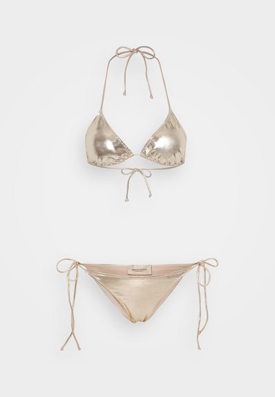 Set di bikini metallizzato oro con coppe triangolari e slip con lacci laterali. Texture liscia con spalline sottili e design minimalista.