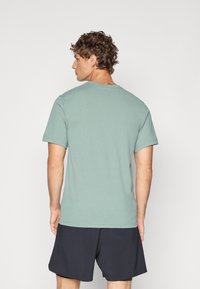 Camiseta de cuello redondo de algodón en un suave tono verde con un corte relajado. Mangas cortas y detalles de costura sutiles, combinada con pantalones cortos oscuros.