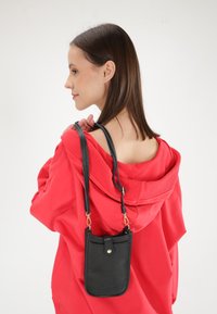 Sort textured læder crossbody taske med gyldne hardware detaljer, der har en lynlåsåbning og en justerbar skulderrem.