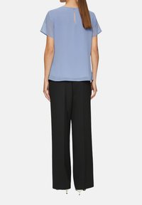 Hellblaues Kurzarmbluse mit einem Schlüsselaugen-Detail auf der Rückseite, kombiniert mit schwarzen weiten Hosen aus glattem Stoff.