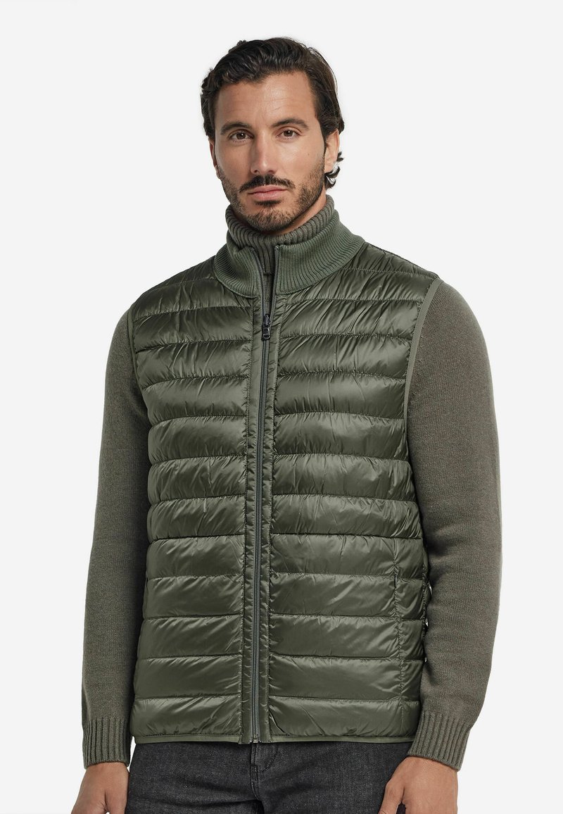 Grön pufferväst med quiltat mönster och hög krage, kombinerad med en stickad olivgrön tröja, som har dragkedja och ribbade mudd.