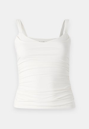 Bílý tílko bez rukávů s výstřihem ve tvaru kulaté lodičky. Obsahuje na bocích nařasenou texturu pro přiléhavý vzhled. Vyrobeno z měkkého, pružného materiálu.