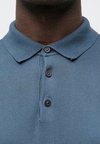 Polo em azul suave, feito de tecido de malha. Apresenta gola com colarinho, pala com três botões e superfície de textura fina.