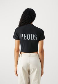 Svart kortärmad t-shirt med ordet "PEQUS" i stora silverfärgade bokstäver på baksidan. Kompletterad med ljusa byxor.