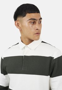 Polo a maniche lunghe a righe verdi e bianche con colletto, cuciture minime e una patta con un solo bottone. Texture in cotone liscia.