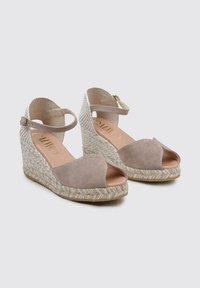 Sandalias de cuña beige con diseño de punta abierta. Parte superior de ante, tacón trenzado, correa en el tobillo con hebilla y detalle de cuerda estampada en la suela.