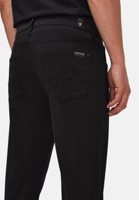 Sorte denimbukser med klassisk fem-lomme design, hævet syning på baglommerne og en glat tekstur. Diskret mærkat synlig.