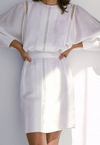 Robe blanche avec des manches ballon, ornée de lignes verticales et d'accents en dentelle. Tissu doux avec une taille cintrée et un ourlet droit.