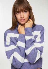 Sweter w paski lawendowy i biały z kołnierzem typu półgolf, charakteryzujący się miękką fakturą i prążkowanymi mankietami. Zbliżenie na odzież.