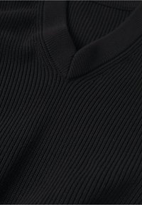 Zwarte gebreide trui met een ribbelstructuur en V-hals ontwerp. Het materiaal lijkt zacht en flexibel, wat de nauwe pasvorm benadrukt.