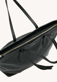 Sac fourre-tout en cuir noir avec deux longues poignées, présentant une fermeture éclair dorée et un détail de gland. Surface texturée, intérieur spacieux.