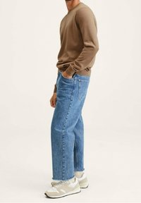 Maglione a maniche lunghe marrone in maglia, jeans in denim blu a forma libera e sneakers beige con dettagli bianchi, visti di lato.