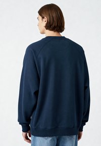Sweat-shirt bleu marine avec un col rond et des manches raglan. Tissu doux avec poignets et ourlet côtelés, présentant un dos lisse et sans ornements.