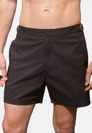 Schwarze Badehosen aus strukturiertem Stoff, mit flachem Bund, seitlichen Taschen und Metallelementen zur Anpassung der Passform.